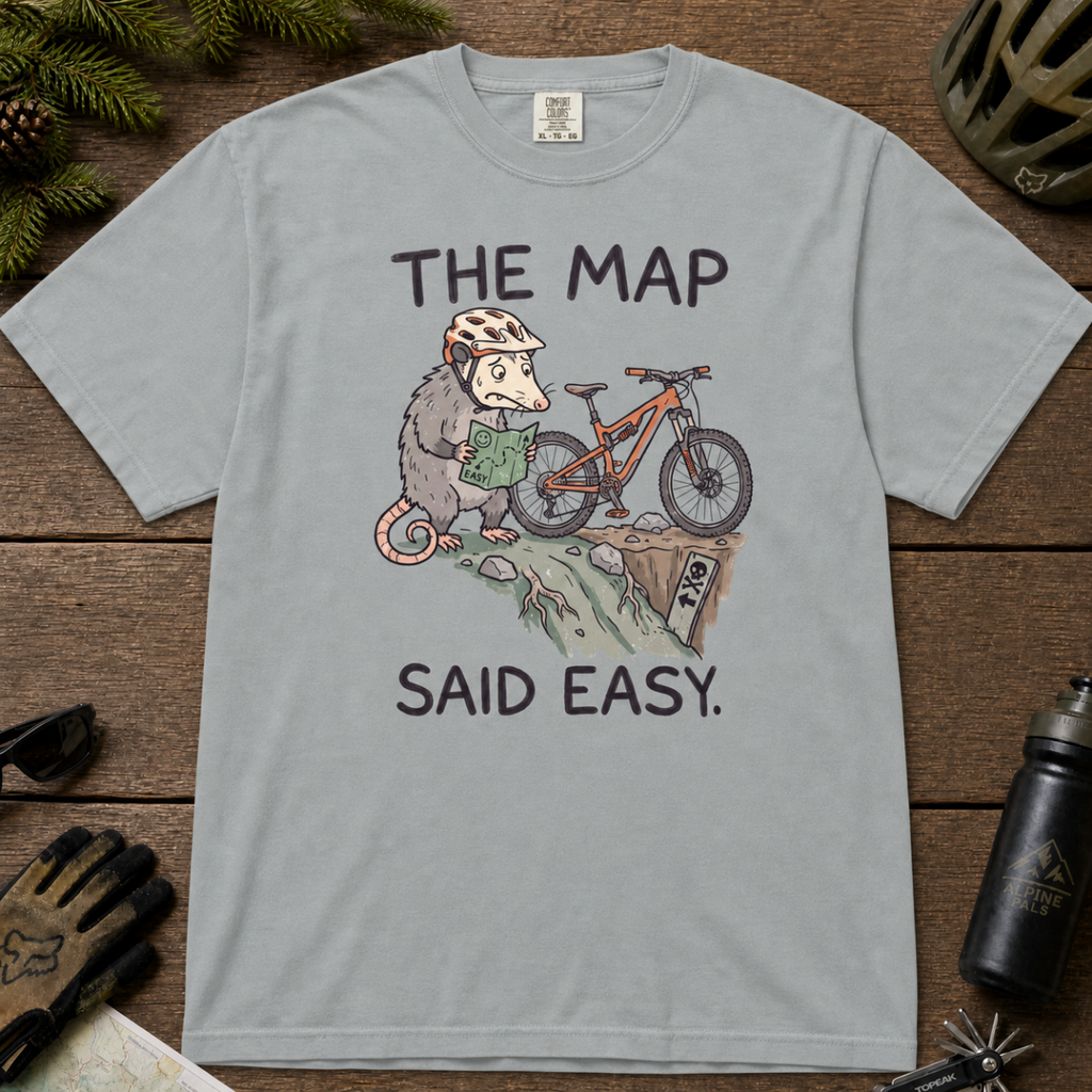 Flat lay of a granite gray t-shirt with a humorous mountain biking design showing a nervous opossum, an orange bike, and a dangerously steep trail.
