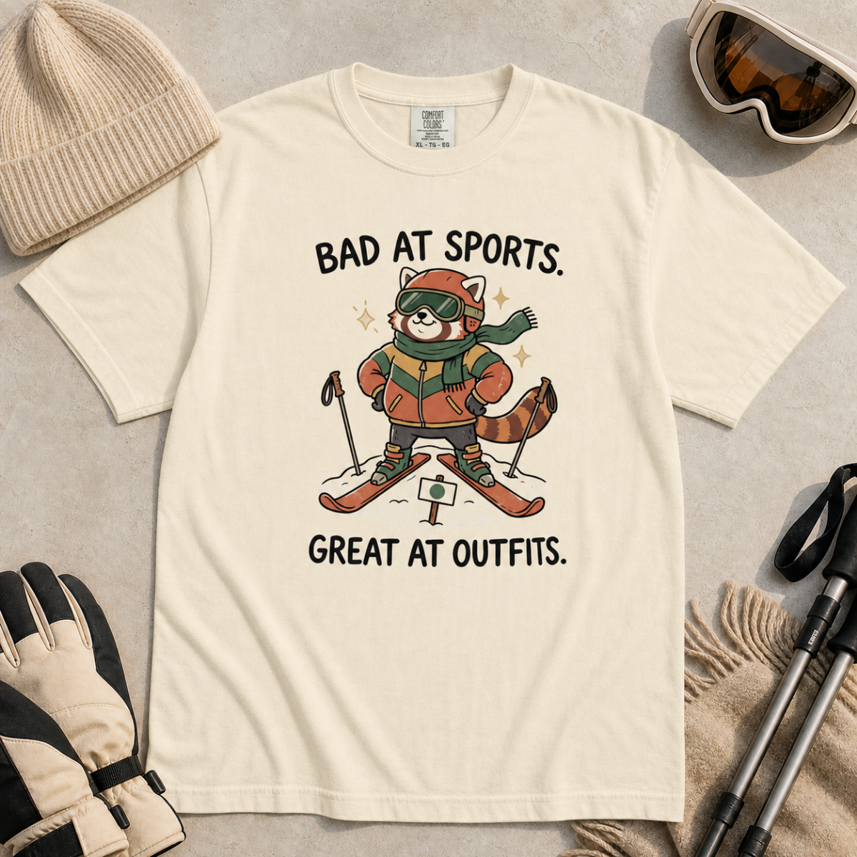 Flat lay of an ivory white t-shirt with a humorous red panda ski design celebrating fashionable gear over athletic ability.