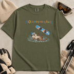 Flat lay of a hemp green t-shirt featuring an upside-down “Is My Snowboard OK?” design with a dazed otter lying in the snow beneath a loose snowboard.