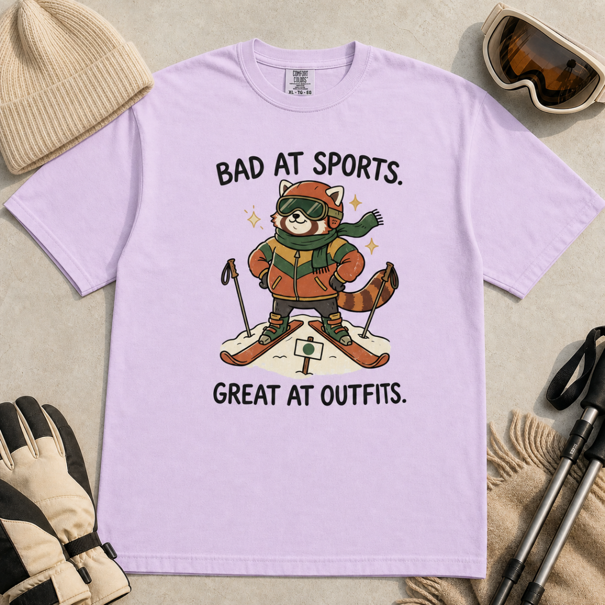 Flat lay of an orchid t-shirt with a humorous red panda ski design celebrating fashionable gear over athletic ability.