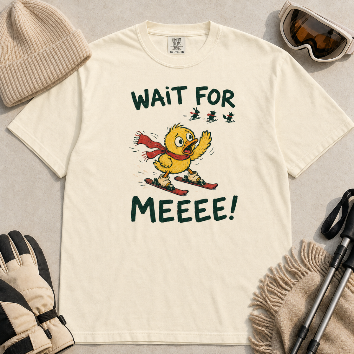 Flat lay of an ivory white t-shirt featuring a panicked duck skiing behind the group with a red scarf and “Wait for Meeee!” text.