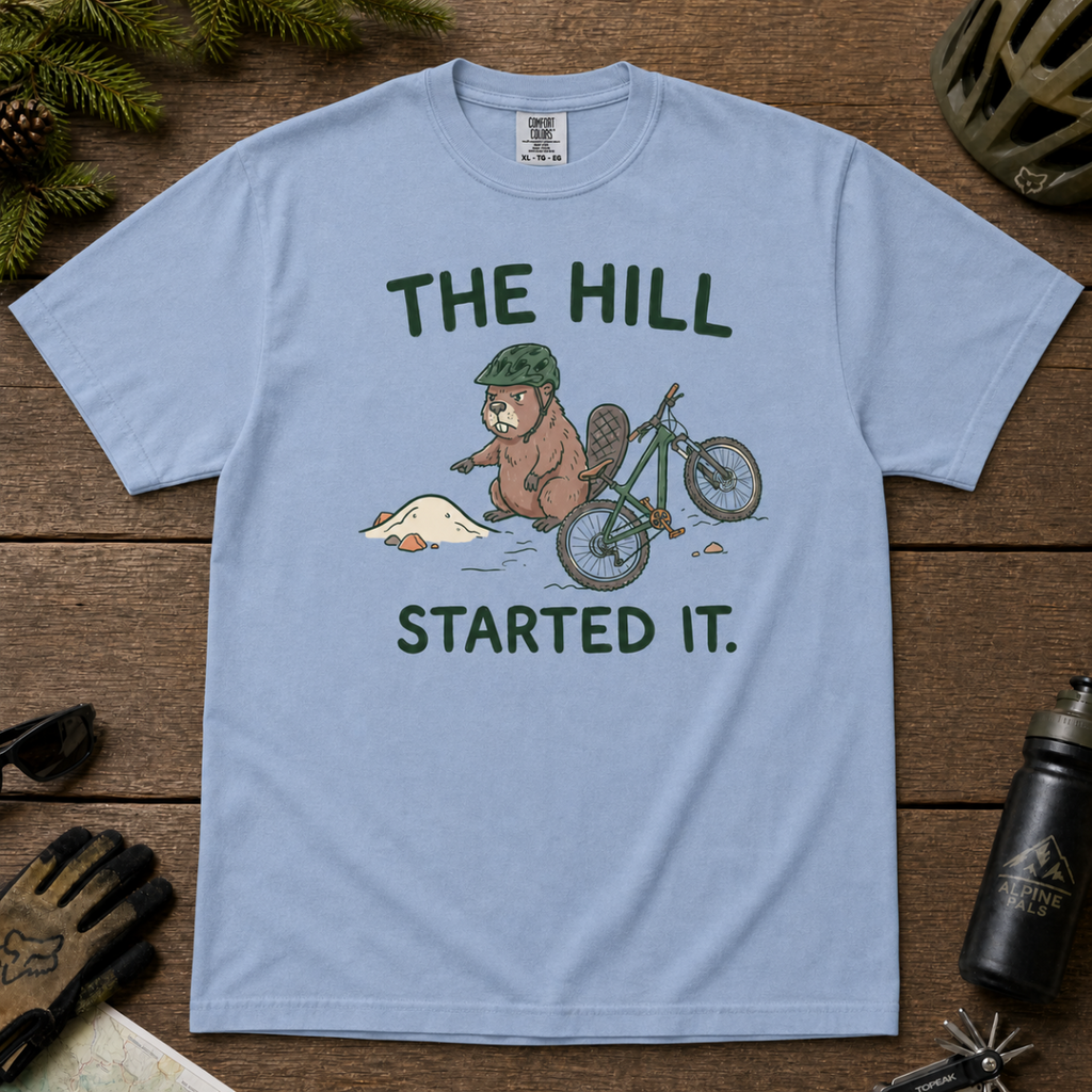 Flat lay of a washed denim blue t-shirt with a humorous mountain biking design showing an annoyed beaver blaming a dirt hill beside its bike.