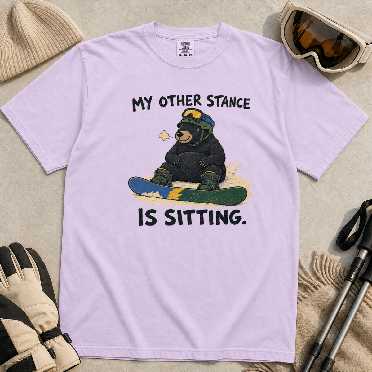Flat lay of an orchid t-shirt with a humorous snowboarding design showing a resting bear seated behind its board.