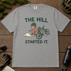 Flat lay of a grey t-shirt with a humorous mountain biking design showing an annoyed beaver blaming a dirt hill beside its bike.