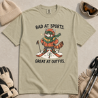 Flat lay of a khaki t-shirt with a humorous red panda ski design celebrating fashionable gear over athletic ability.