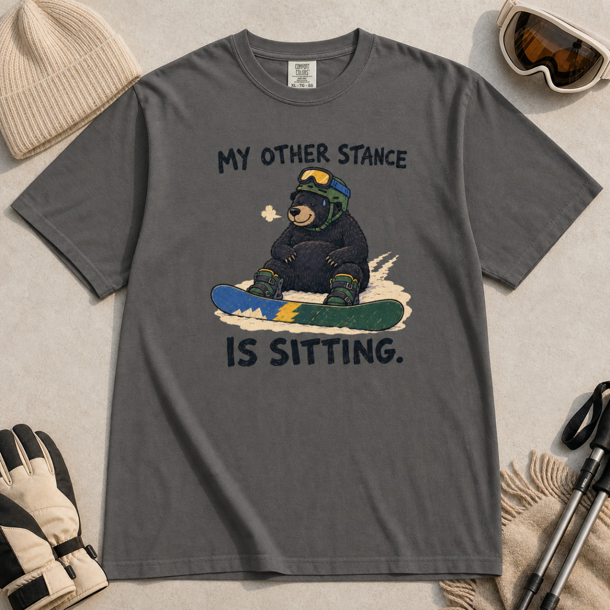 Flat lay of a pepper gray t-shirt with a humorous snowboarding design showing a resting bear seated behind its board.