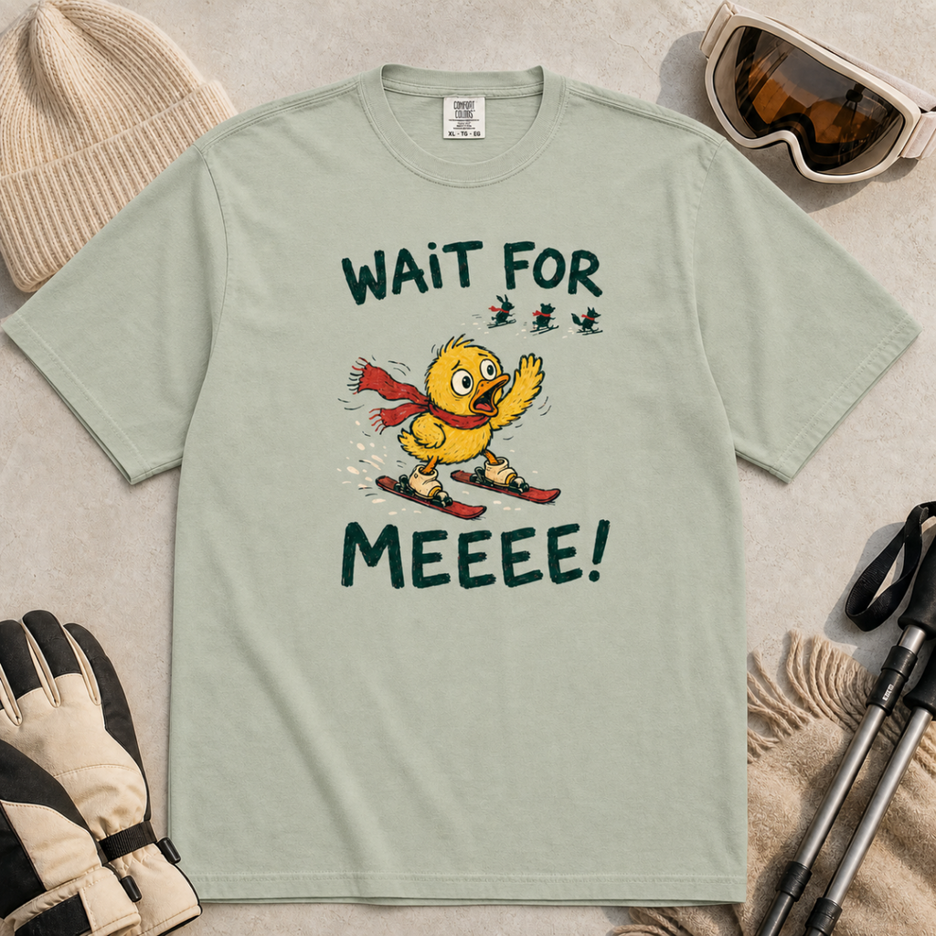 Flat lay of a bay green t-shirt featuring a panicked duck skiing behind the group with a red scarf and “Wait for Meeee!” text.