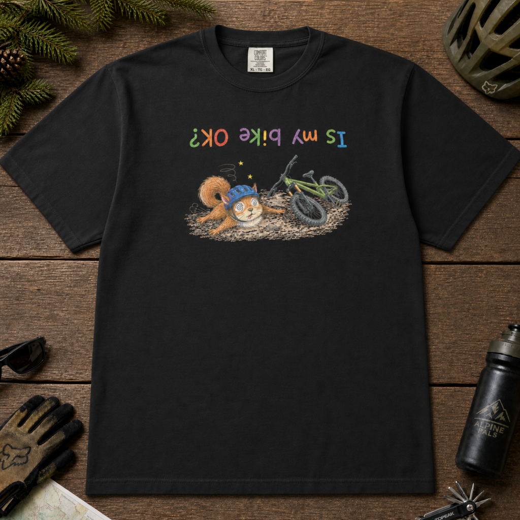Flat lay of a black t-shirt featuring a humorous squirrel mountain bike crash design with an upside-down “Is My Bike OK?” message.