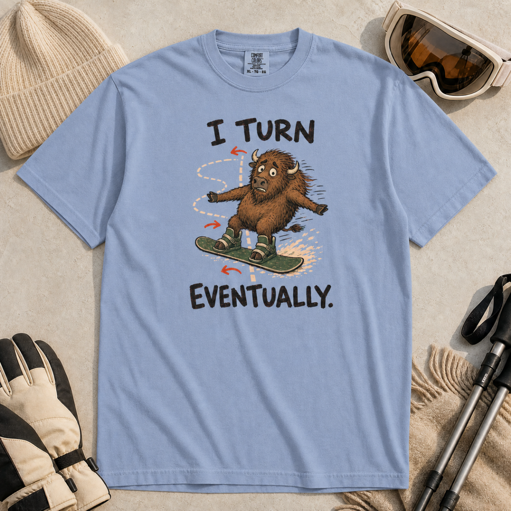 Flat lay of a washed denim blue t-shirt featuring a nervous bison snowboarding along a winding path with “I Turn Eventually.” text.