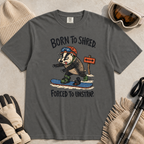Flat lay of a pepper gray t-shirt featuring a frustrated badger snowboarder removing one foot from its binding, with “Born to Shred. Forced to Unstrap.” text.
