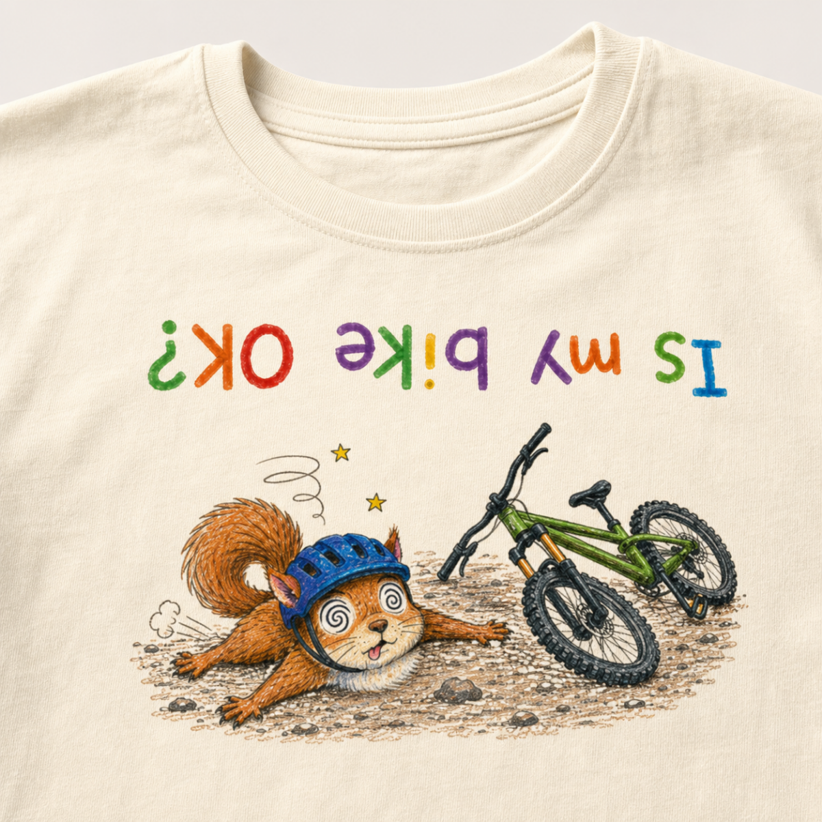 Close-up of an ivory white t-shirt showing a dazed squirrel after a mountain bike crash beside a green bike, with colourful upside-down “Is My Bike OK?” text.