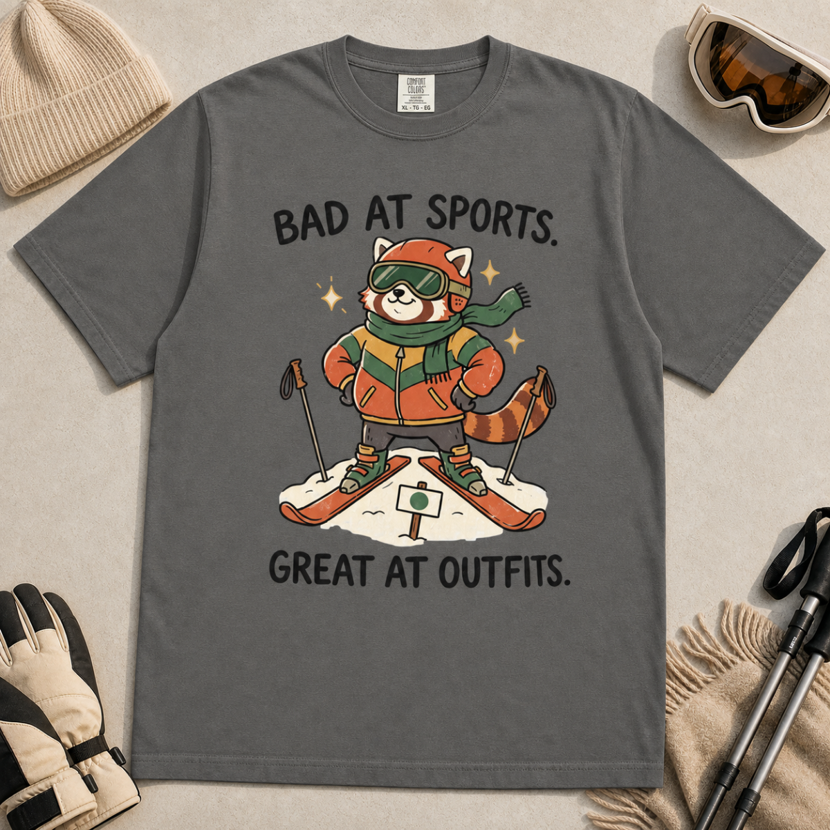 Flat lay of a pepper gray t-shirt with a humorous red panda ski design celebrating fashionable gear over athletic ability.