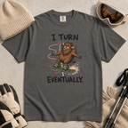 Flat lay of a pepper gray t-shirt featuring a nervous bison snowboarding along a winding path with “I Turn Eventually.” text.