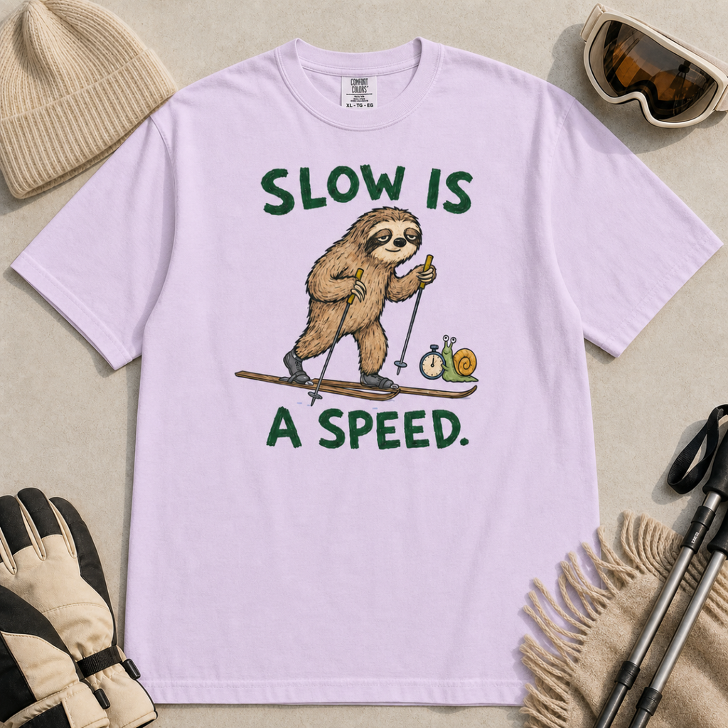 Flat lay of an orchid t-shirt with a humorous sloth skiing graphic, a stopwatch-holding snail, and bold green “Slow Is a Speed.” text.