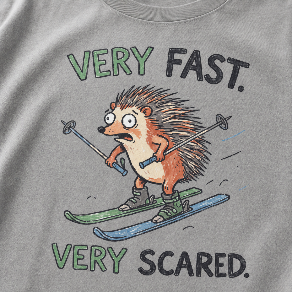 Close-up of a grey t-shirt with a playful hedgehog ski graphic showing the wide-eyed animal racing downhill with poles and mismatched skis.