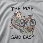 Close-up of a granite gray t-shirt featuring a worried opossum checking an “easy” trail map beside a mountain bike at a steep drop, with “The Map Said Easy.” text.