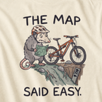 Close-up of an ivory white t-shirt featuring a worried opossum checking an “easy” trail map beside a mountain bike at a steep drop, with “The Map Said Easy.” text.