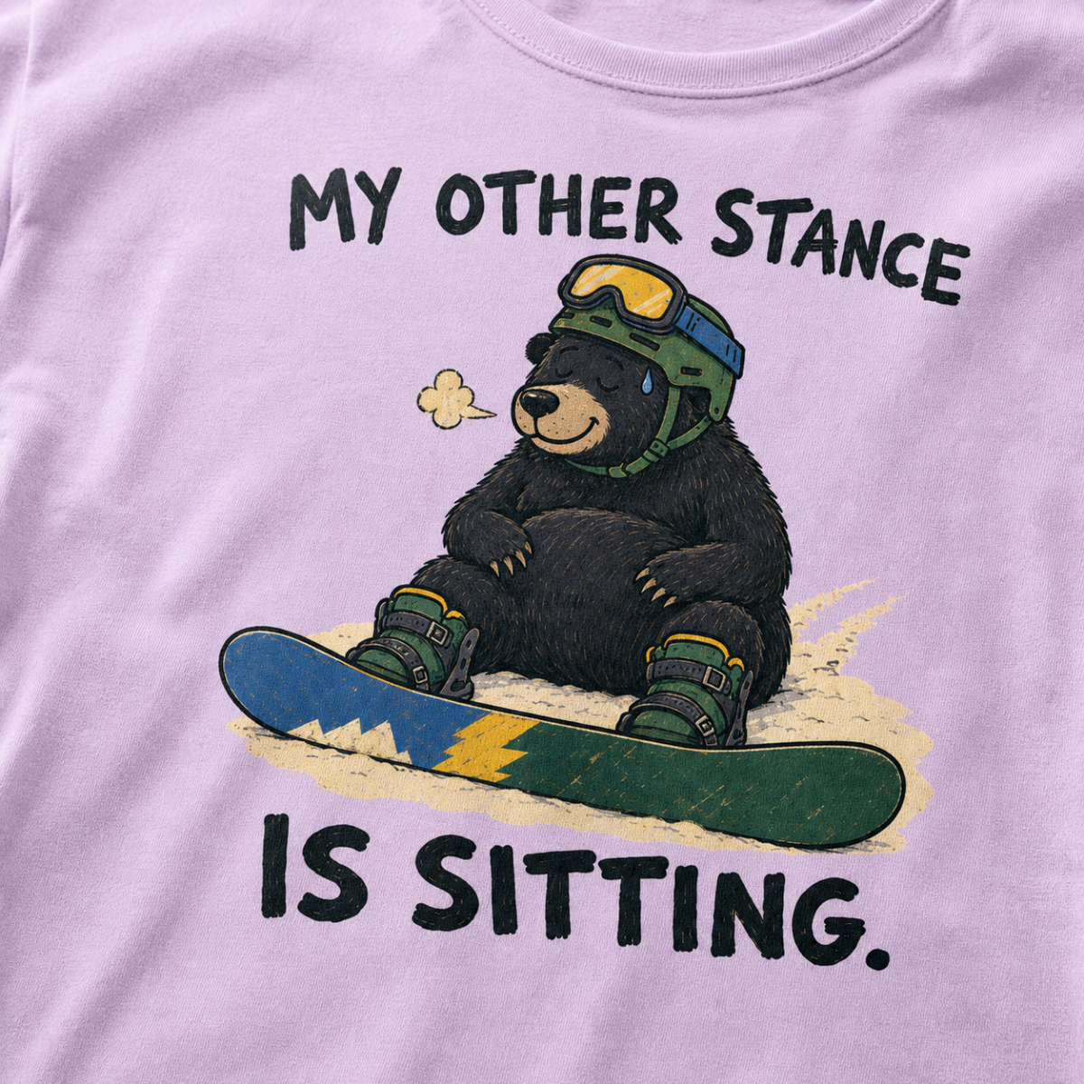 Close-up of an orchid t-shirt featuring a tired bear sitting in the snow beside a snowboard, with “My Other Stance Is Sitting.” text.