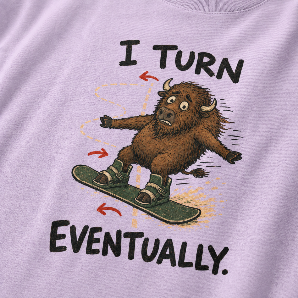 Close-up of an orchid t-shirt showing a wide-eyed bison struggling to steer a snowboard, with directional arrows and “I Turn Eventually.” text.