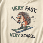 Close-up of an ivory white t-shirt with a playful hedgehog ski graphic showing the wide-eyed animal racing downhill with poles and mismatched skis.