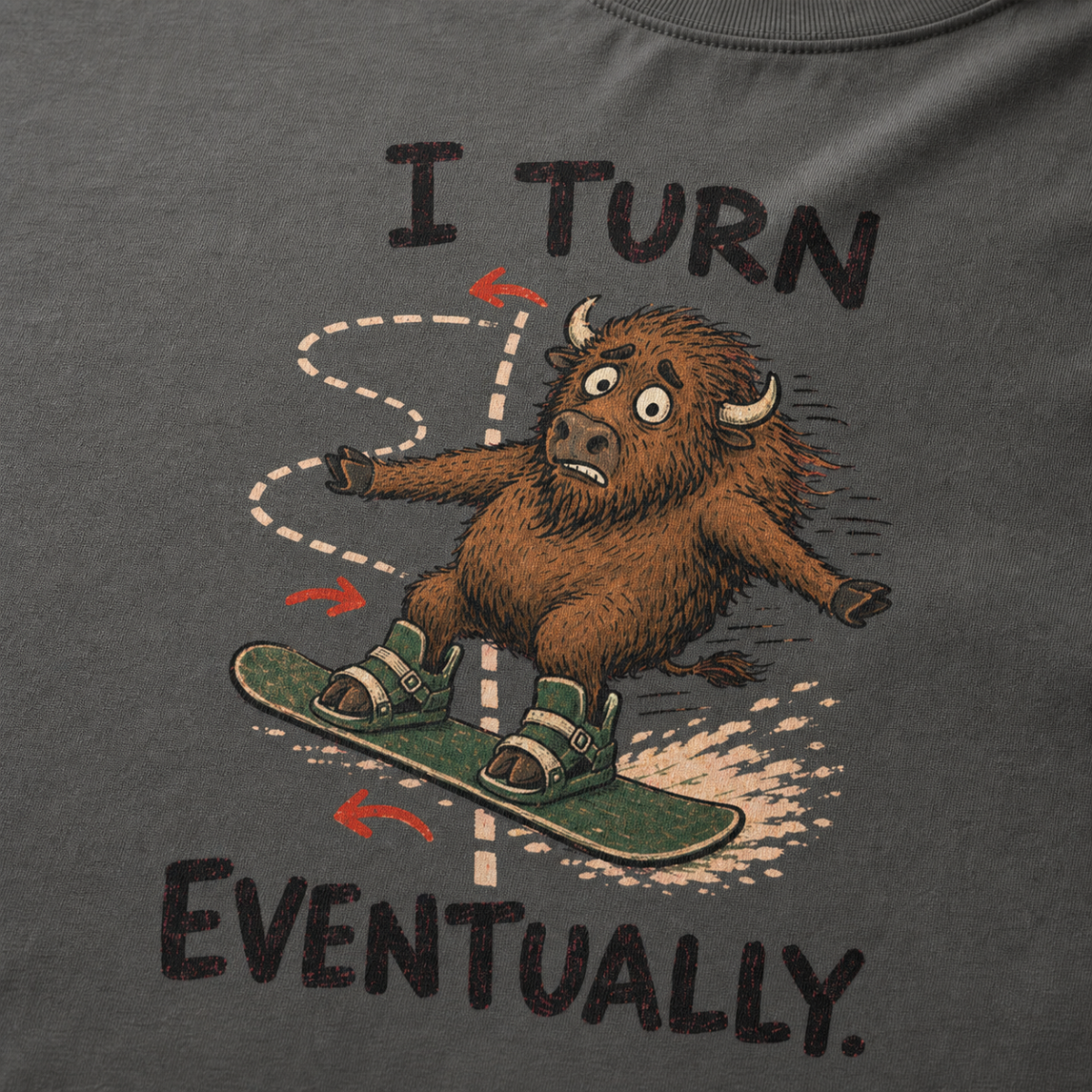 Close-up of a pepper gray t-shirt showing a wide-eyed bison struggling to steer a snowboard, with directional arrows and “I Turn Eventually.” text.