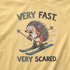 Close-up of a butter yellow t-shirt with a playful hedgehog ski graphic showing the wide-eyed animal racing downhill with poles and mismatched skis.