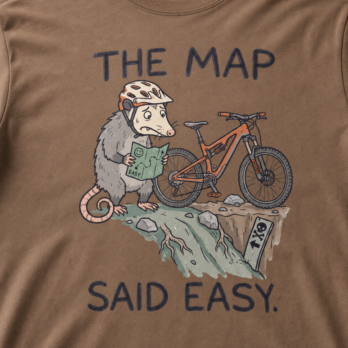 Close-up of an espresso brown t-shirt featuring a worried opossum checking an “easy” trail map beside a mountain bike at a steep drop, with “The Map Said Easy.” text.