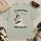 Flat lay of a bay green t-shirt with a humorous snowboarding design showing a worried rabbit facing an unexpectedly steep jump.