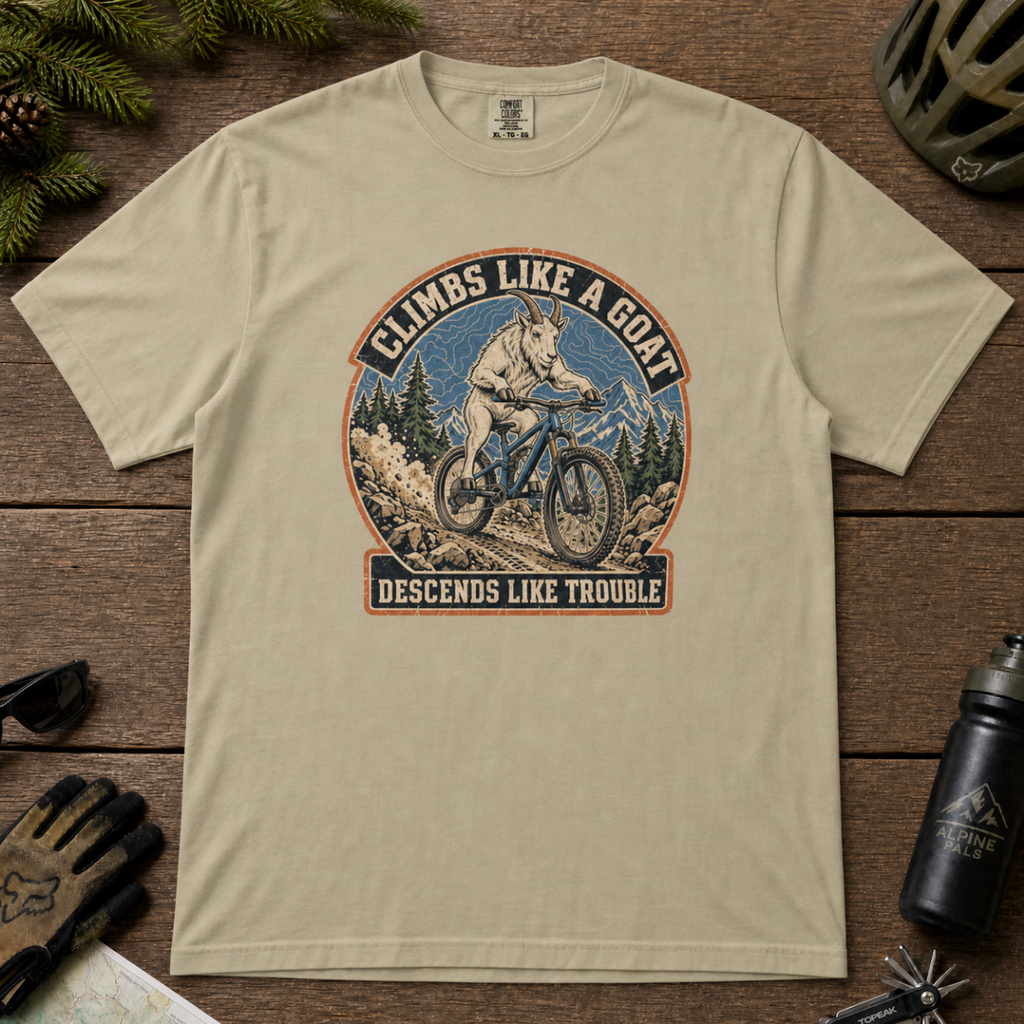 Khaki t-shirt featuring a vintage mountain goat riding a mountain bike through rocky alpine terrain with “Climbs Like a Goat, Descends Like Trouble” text.