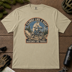 Khaki t-shirt featuring a vintage mountain goat riding a mountain bike through rocky alpine terrain with “Climbs Like a Goat, Descends Like Trouble” text.