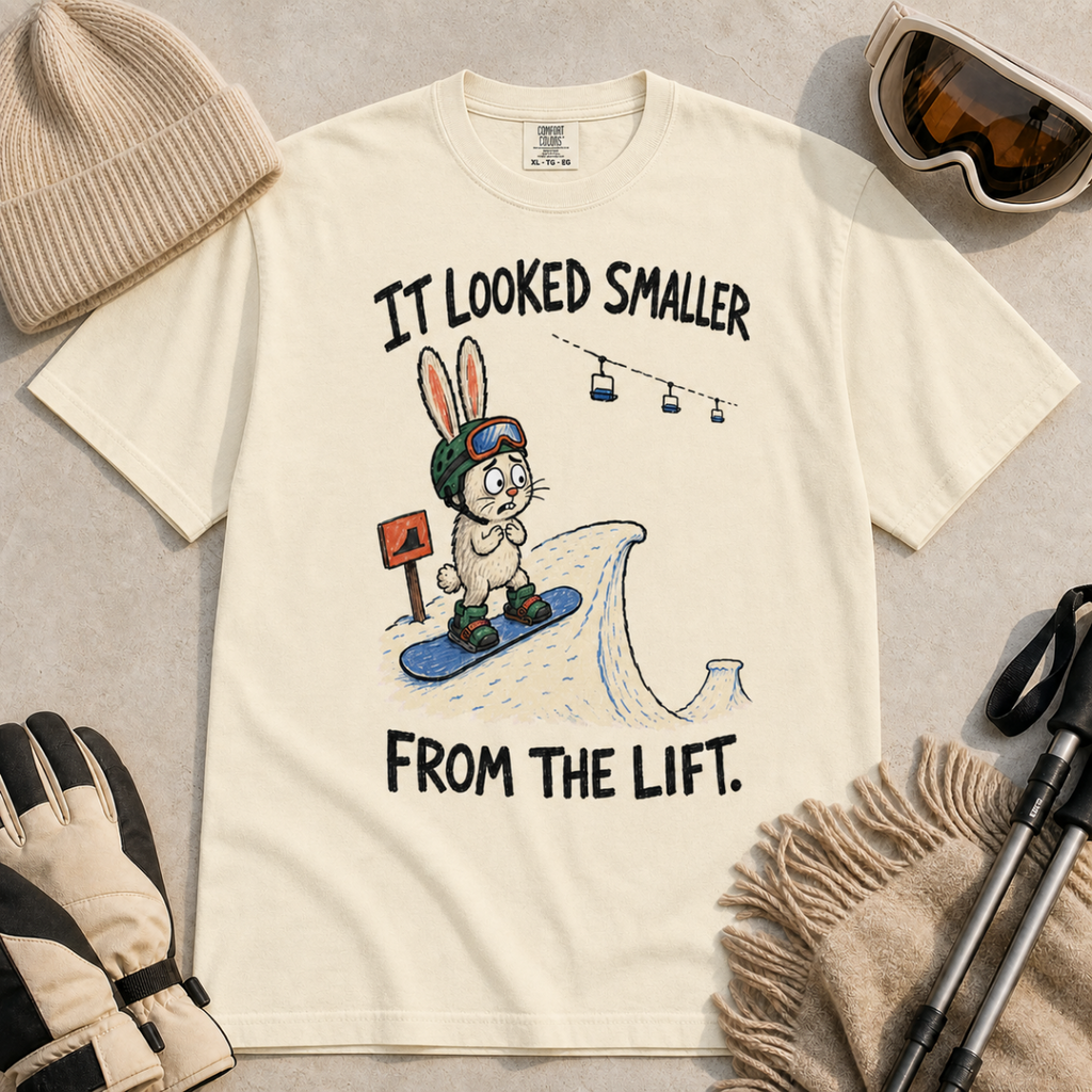 Flat lay of an ivory white t-shirt with a humorous snowboarding design showing a worried rabbit facing an unexpectedly steep jump.
