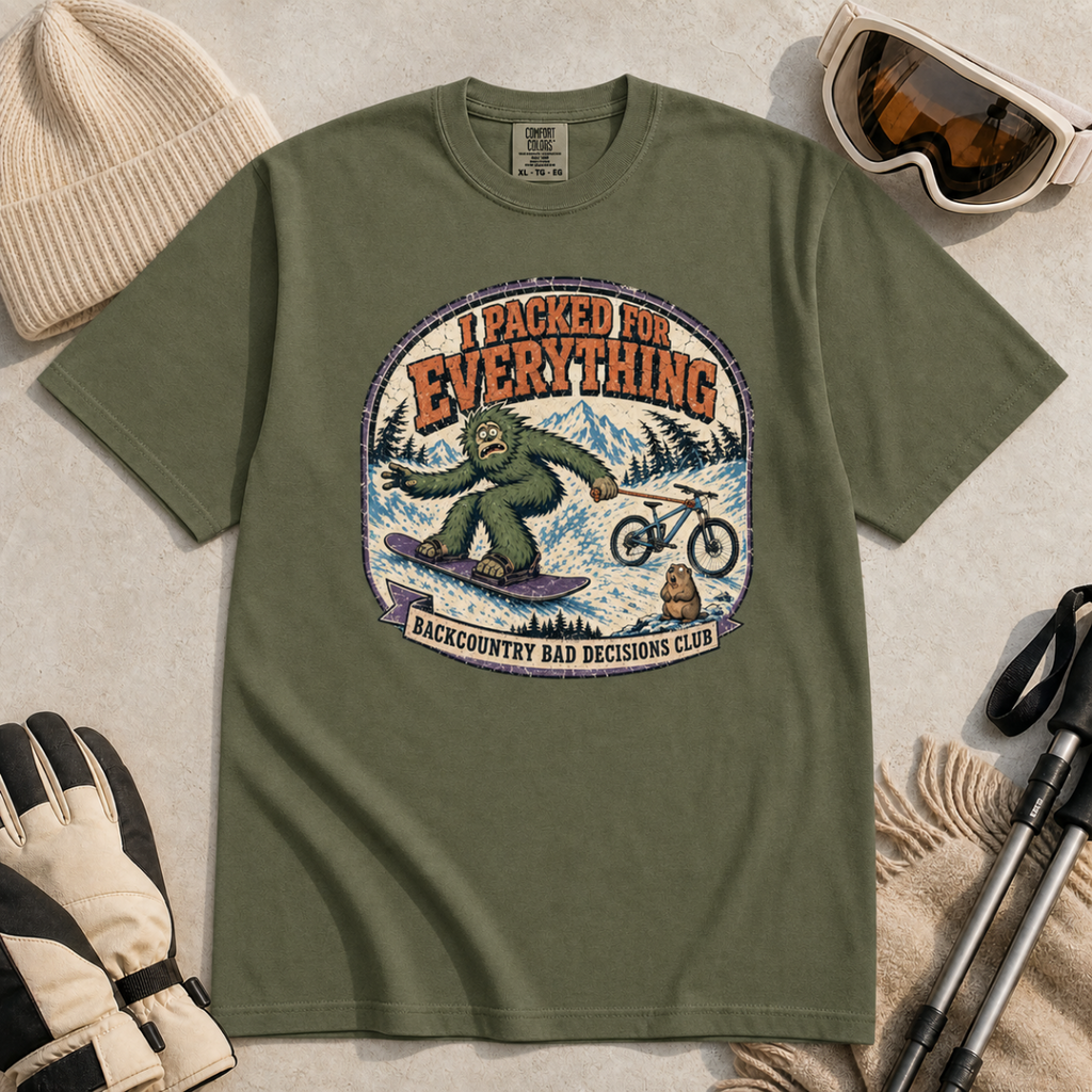 Hemp green t-shirt featuring a vintage backcountry badge design with Bigfoot snowboarding, a mountain bike, snowy peaks, and “I Packed for Everything” lettering.