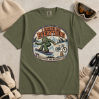 Hemp green t-shirt featuring a vintage backcountry badge design with Bigfoot snowboarding, a mountain bike, snowy peaks, and “I Packed for Everything” lettering.