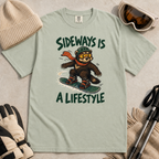 Flat lay of a bay green t-shirt with a playful wolverine snowboard graphic and bold “Sideways Is a Lifestyle” text.