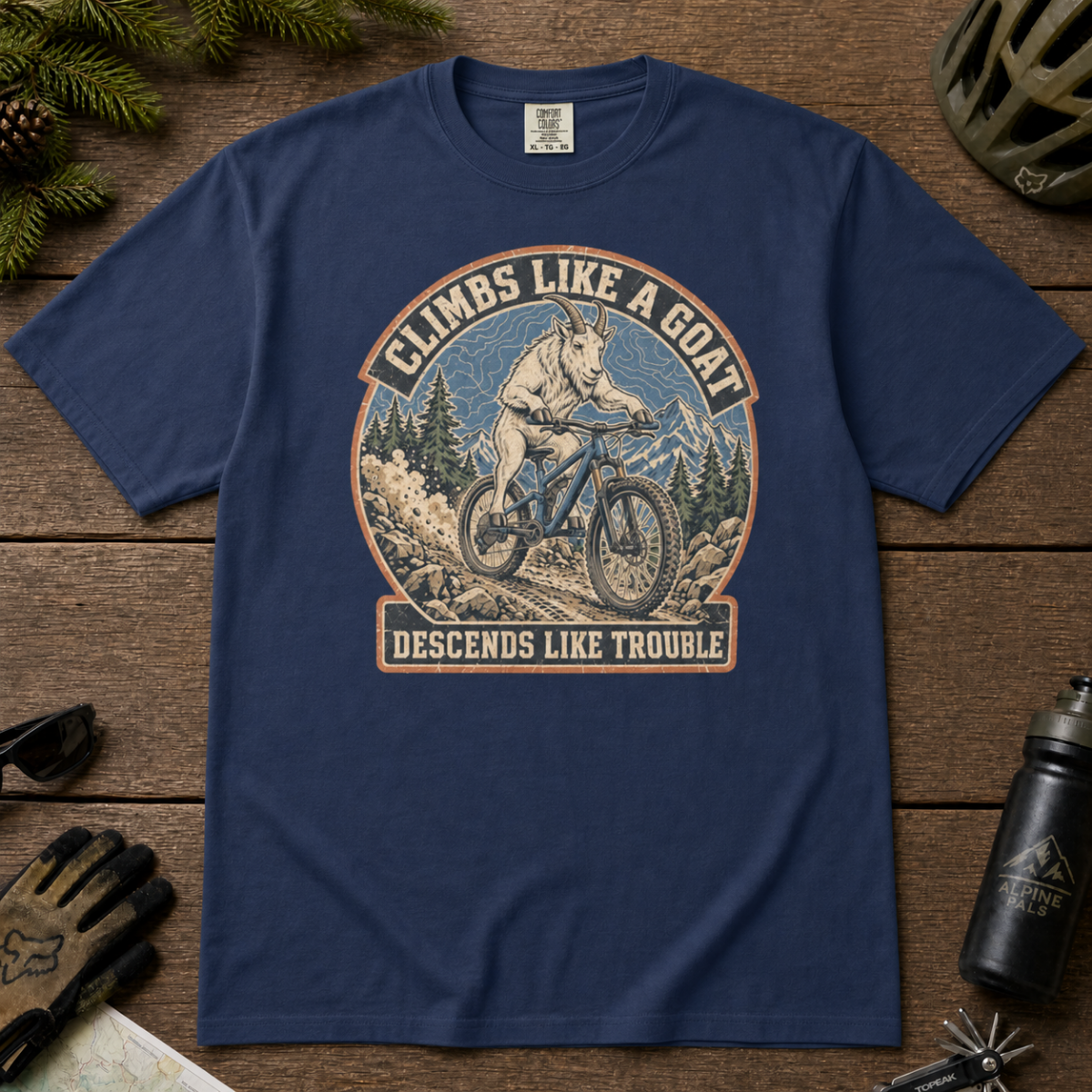 Navy blue t-shirt featuring a vintage mountain goat riding a mountain bike through rocky alpine terrain with “Climbs Like a Goat, Descends Like Trouble” text.