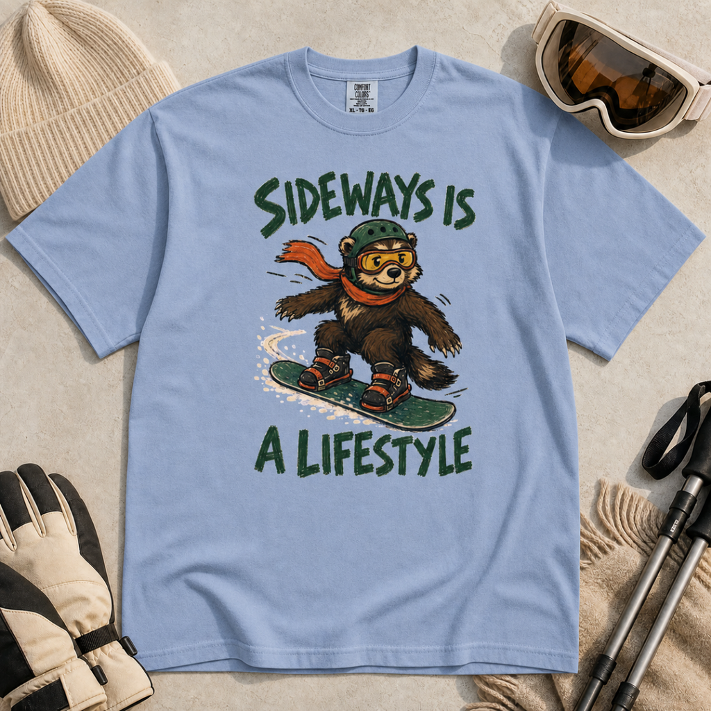 Flat lay of a washed denim blue t-shirt with a playful wolverine snowboard graphic and bold “Sideways Is a Lifestyle” text.