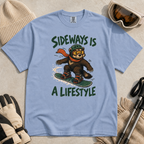 Flat lay of a washed denim blue t-shirt with a playful wolverine snowboard graphic and bold “Sideways Is a Lifestyle” text.