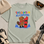 Flat lay of a bay green t-shirt with a playful beaver snowboarding design showing the animal chewing a board beneath “This Counts as Carving” text.
