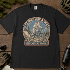 Black t-shirt featuring a vintage mountain goat riding a mountain bike through rocky alpine terrain with “Climbs Like a Goat, Descends Like Trouble” text.