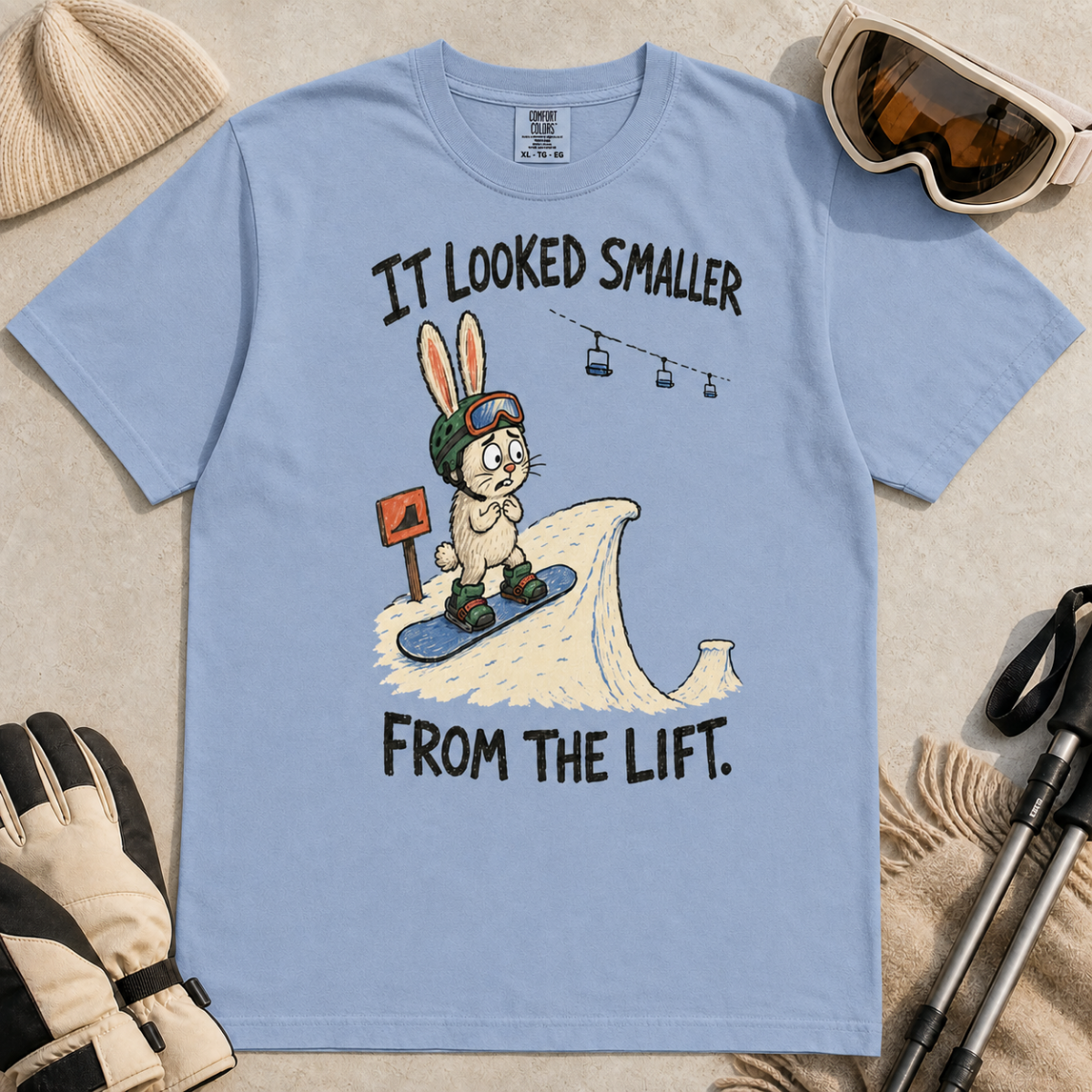 Flat lay of a washed denim blue t-shirt with a humorous snowboarding design showing a worried rabbit facing an unexpectedly steep jump.