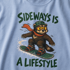 Close-up of a washed denim blue t-shirt featuring a wolverine snowboarding sideways in a helmet, goggles, and red scarf, with “Sideways Is a Lifestyle” text.