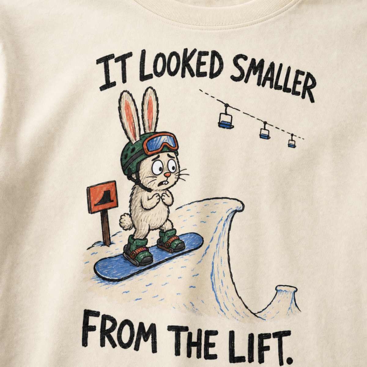Close-up of an ivory white t-shirt featuring a nervous rabbit snowboarder at the edge of a large snow jump, with “It Looked Smaller From the Lift.” text.