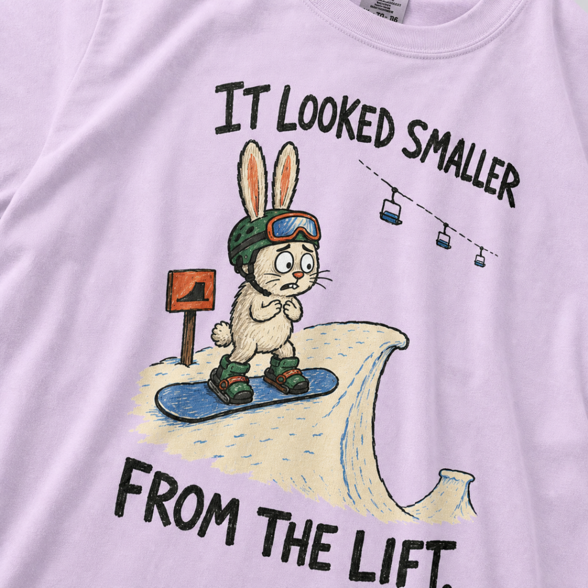 Close-up of an orchid t-shirt featuring a nervous rabbit snowboarder at the edge of a large snow jump, with “It Looked Smaller From the Lift.” text.