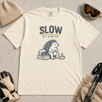 Ivory white t-shirt featuring a seated hedgehog beside ski goggles and a hot drink beneath “Slow by Choice” text.