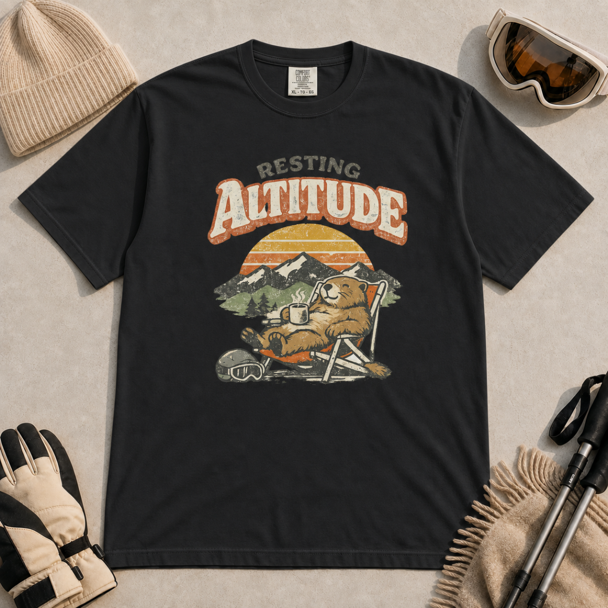 Black t-shirt featuring a marmot resting in a chair with a mug, ski helmet and goggles beneath “Resting Altitude” text.