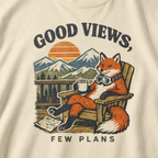 Close-up of an ivory white t-shirt design showing a fox relaxing with a mug before mountain scenery and the phrase “Good Views, Few Plans.”