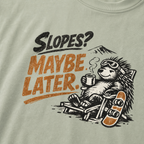 Close-up of a reclining hedgehog holding a hot drink beside a snowboard with “Slopes? Maybe Later.” lettering.