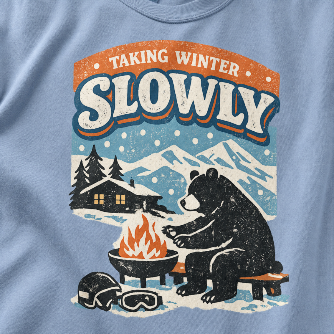Close-up of a bear sitting beside a winter fire with snowy mountains, a cabin, helmet and goggles.