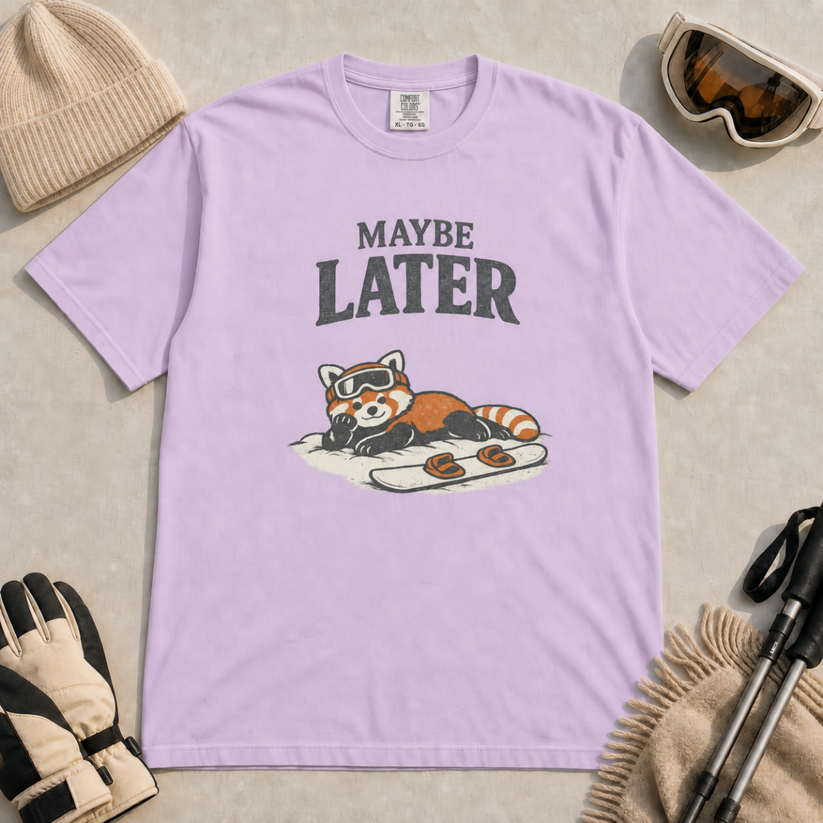 Orchid purple t-shirt featuring a relaxed red panda in ski goggles lying beside a snowboard beneath the words “Maybe Later.”