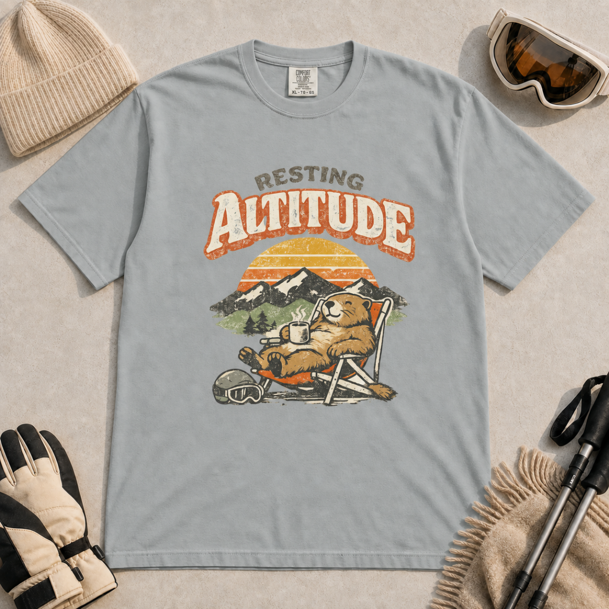 Granite gray t-shirt featuring a marmot resting in a chair with a mug, ski helmet and goggles beneath “Resting Altitude” text.